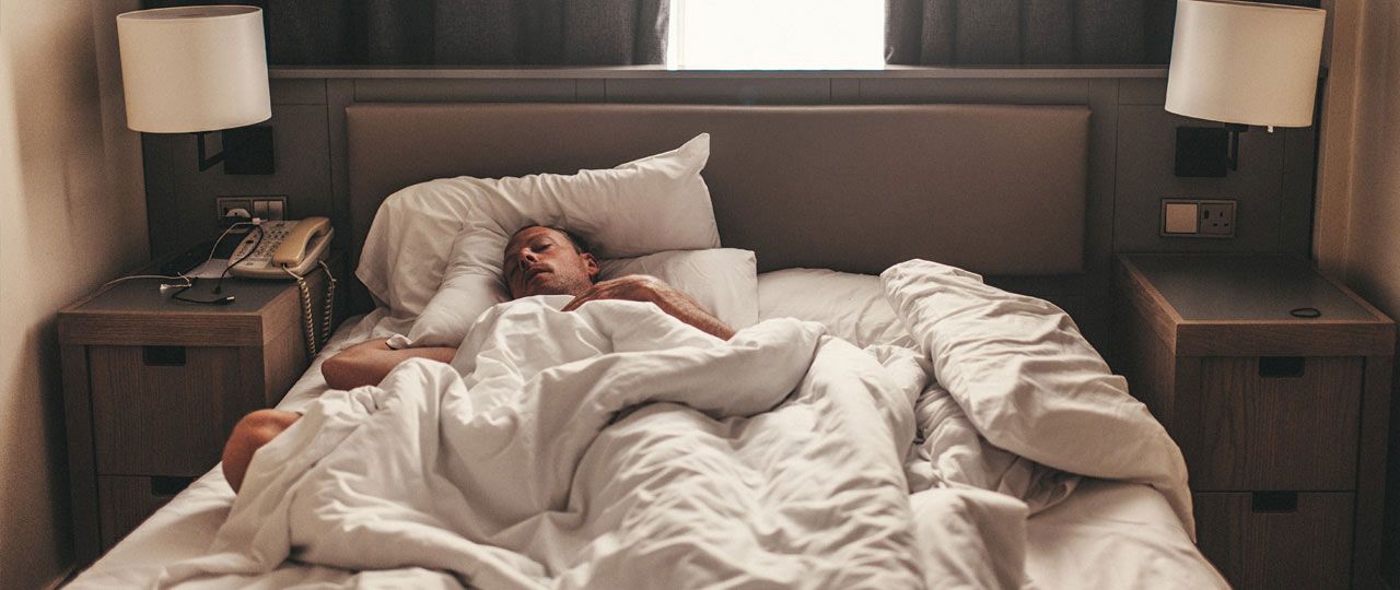 Ein Mann liegt krank mit Fieber im Hotelbett.