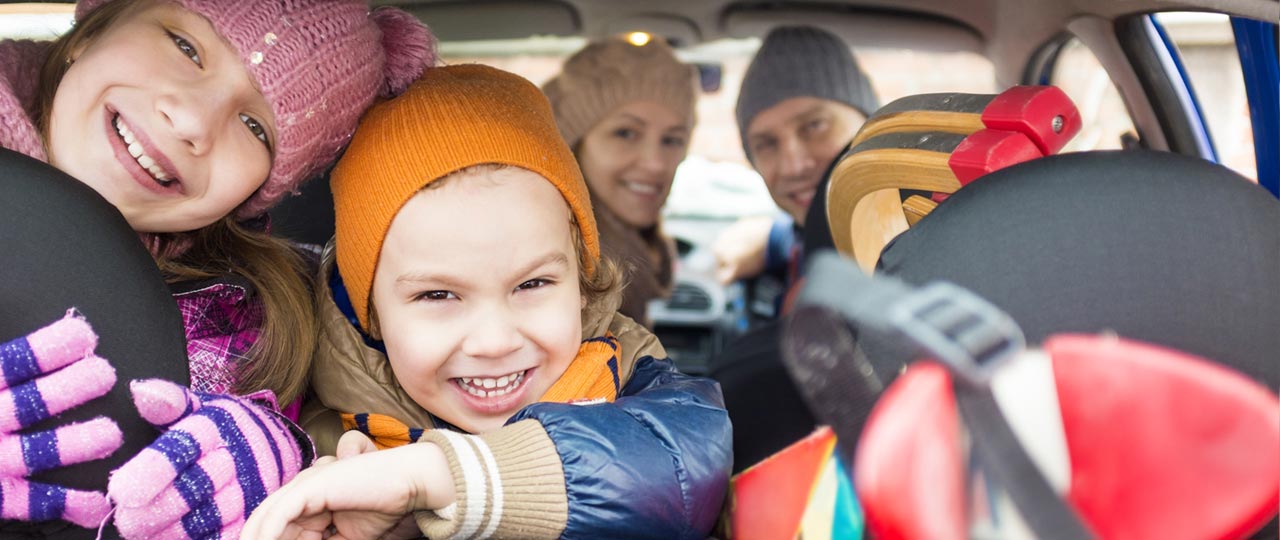 Lachende Familie mit zwei Kindern im Auto. Sie fahren in den Winterurlaub.