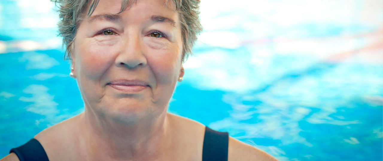 Eine Frau mit Badeanzug in einem Schwimmbecken lächelt.