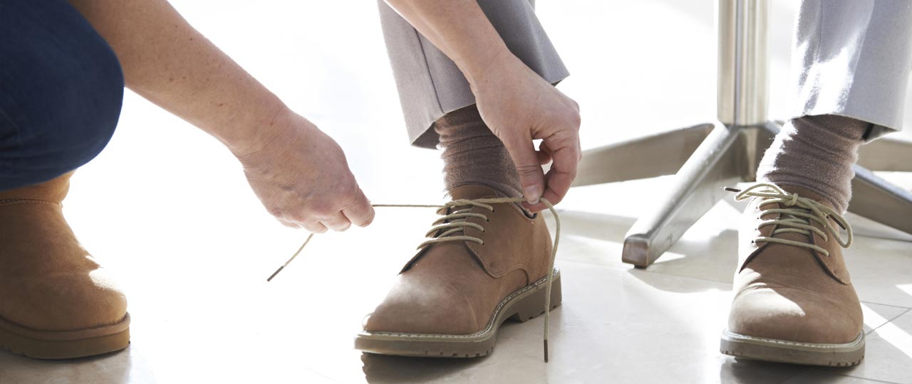 Eine Frau bindet einem Mann die Schuhe zu.