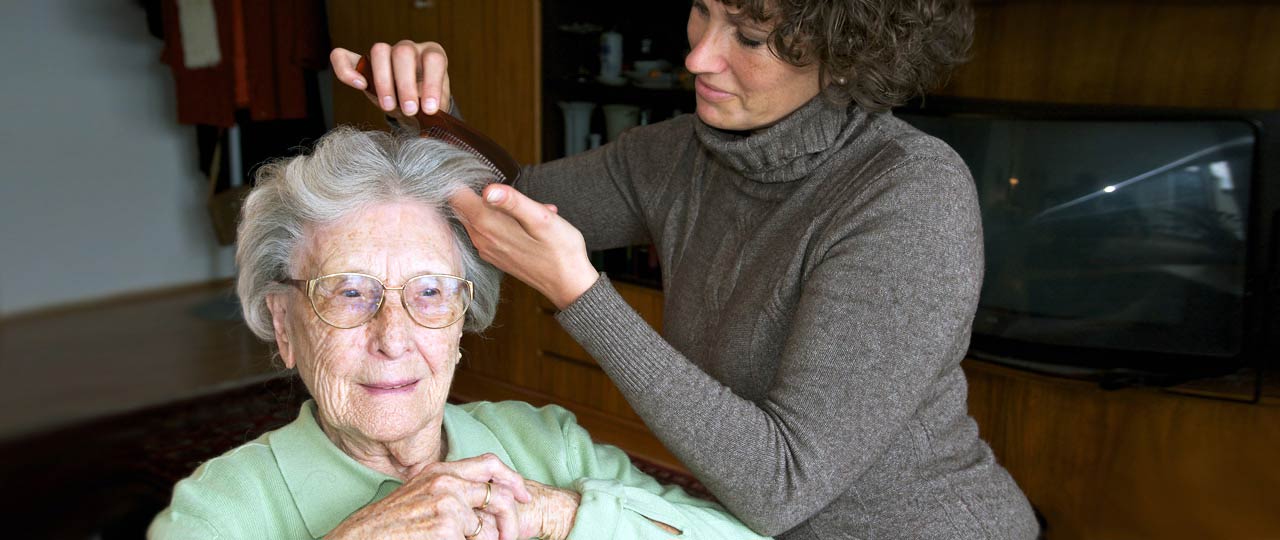 Eine Pflegerin kämmt einer älteren Dame die Haare.