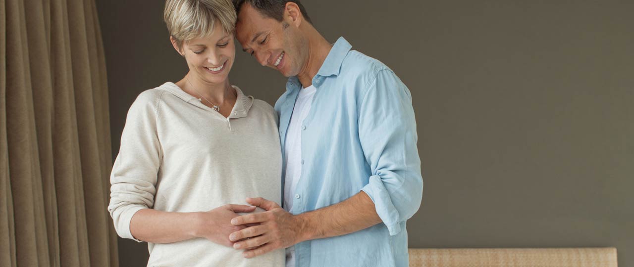 Ein Paar freut sich auf die bevorstehende Geburt. Beide legen die Hände auf den Bauch der Frau.