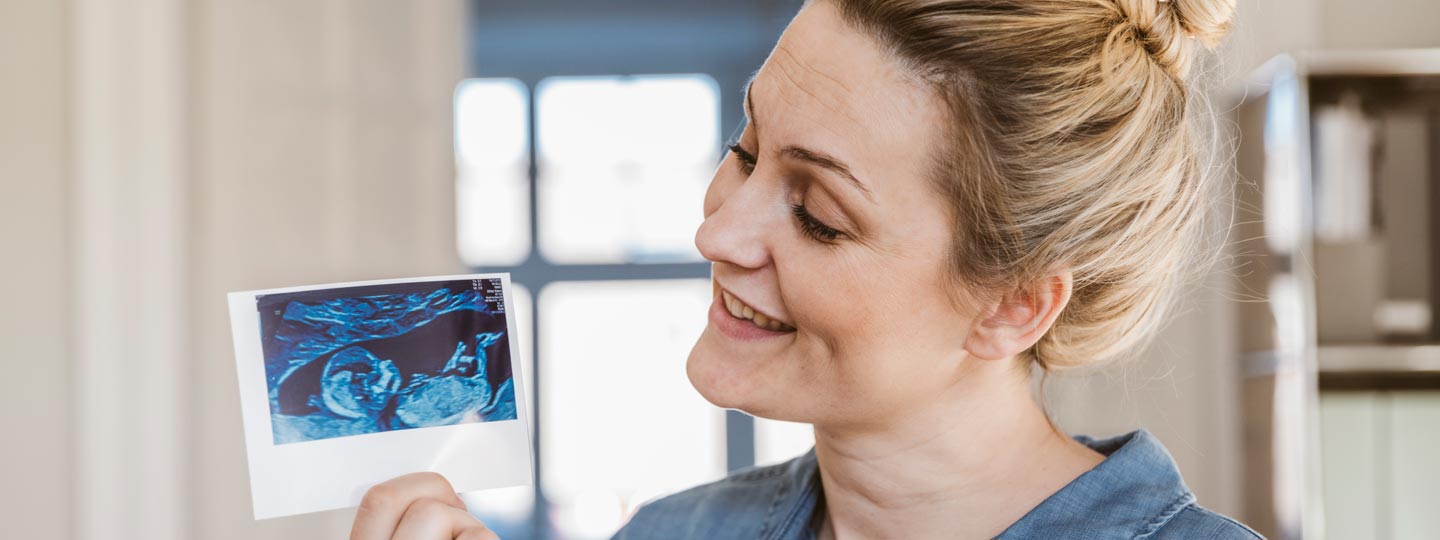 Eine glückliche junge Mutter hält ein Ultraschall-Bild in die Kamera.