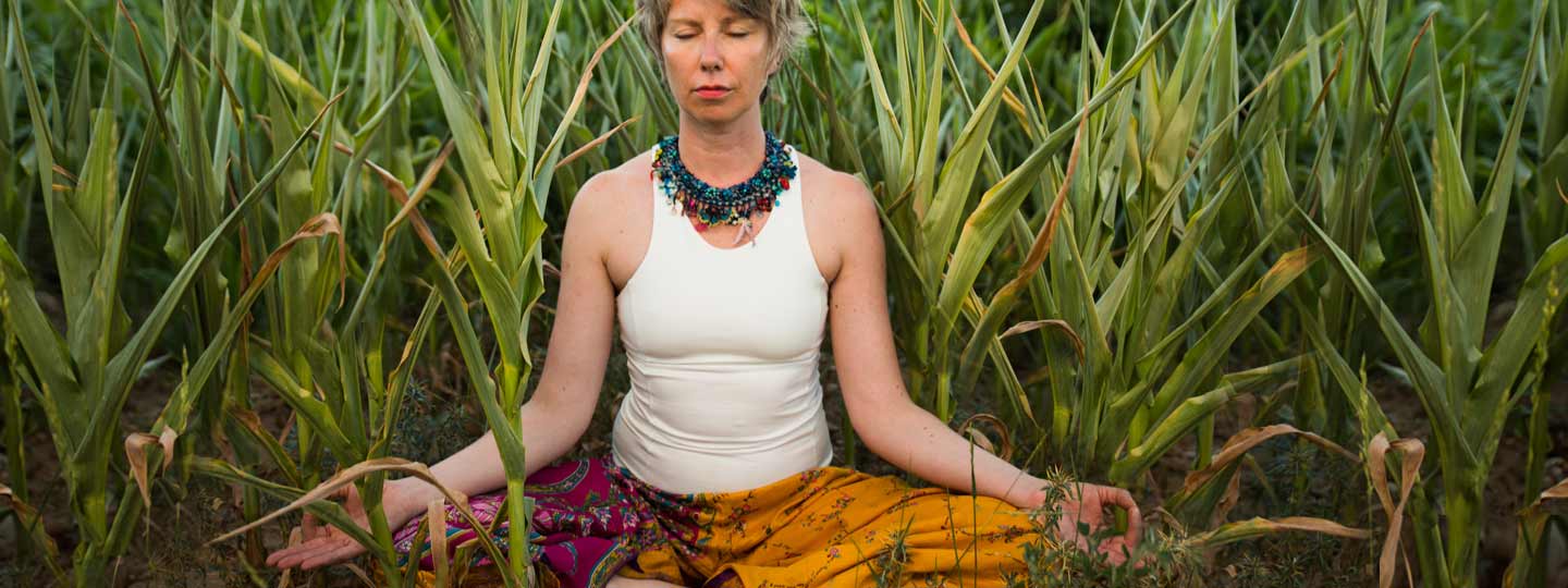 Eine Frau meditiert in einem Maisfeld.