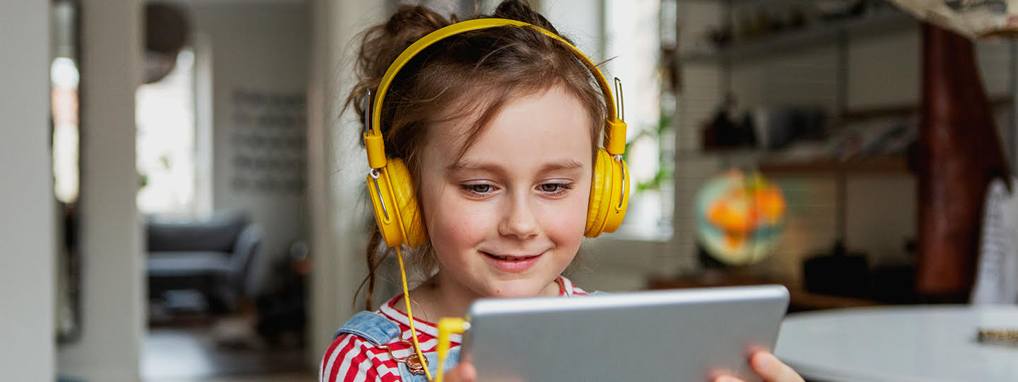 Ein Mädchen mit einem Tablet in der Hand und Kopfhörer auf den Ohren.