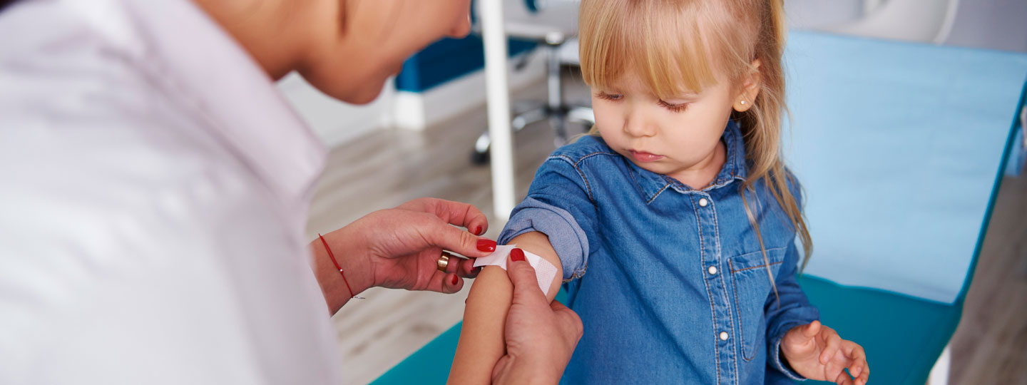 Eine Ärztin klebt ein Pflaster auf den Arm eines kleinen Mädchens nach ihrer Impfung.