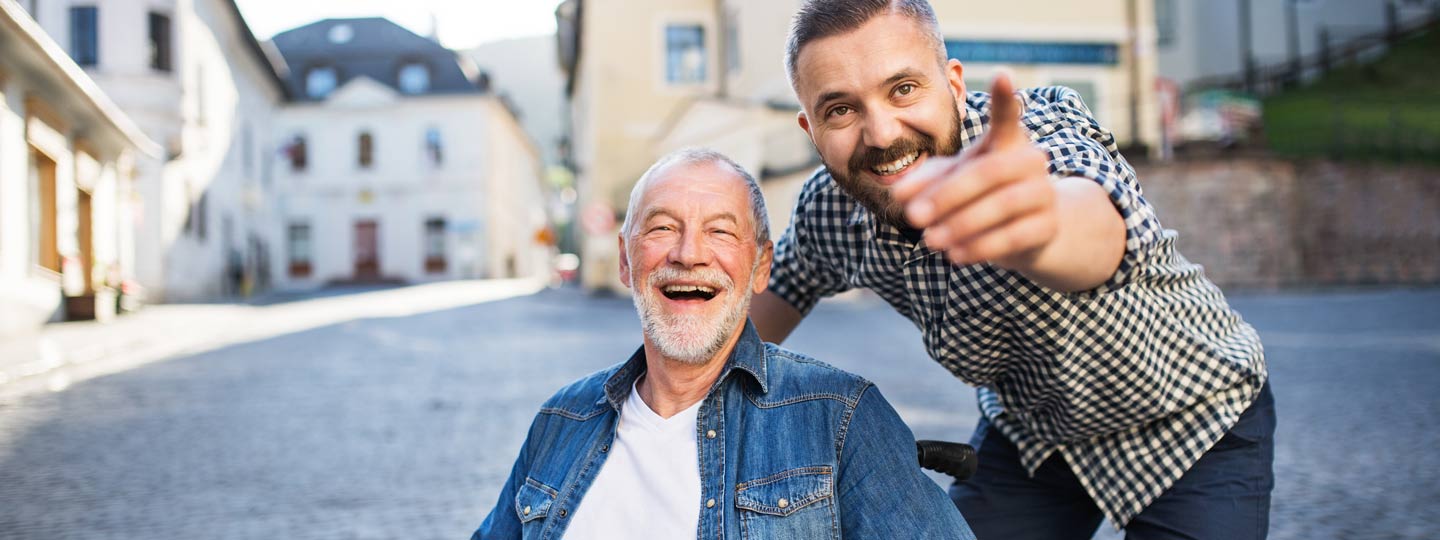 Ein glücklicher, älterer Herr im Rollstuhl bei einem Ausflug mit seinem Pfleger.