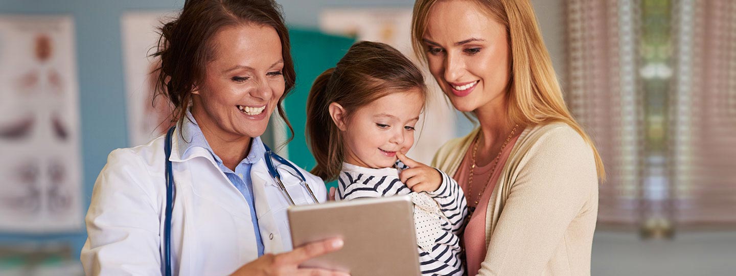 Eine Ärztin zeigt einer jungen Mutter und ihrem kleinen Kind etwas auf einem Tablet.