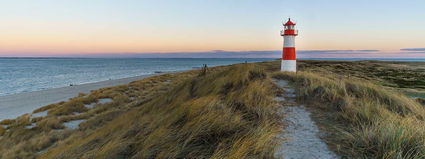 Ein Leuchtturm auf einer Dühne am Meer bei Sonnenaufgang.