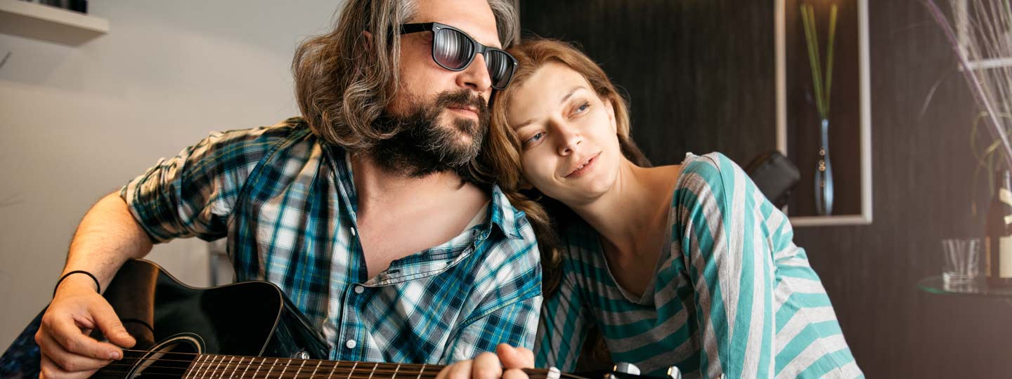 Ein Mann spielt auf einer Gitarre, während eine Frau verträumt an seiner Schulter lehnt.
