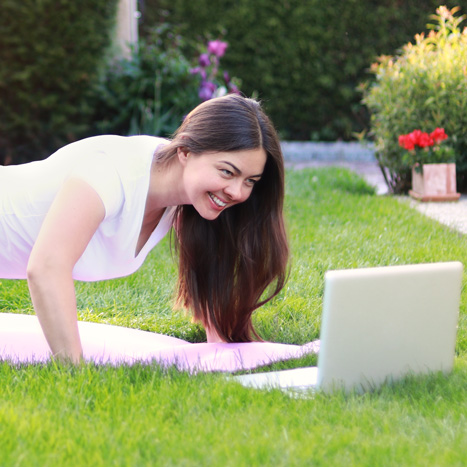 Eine Frau nimmt am Onlin-Kurs Abjetzt/Fit, vor einem Laptop in ihrem Garten, teil.