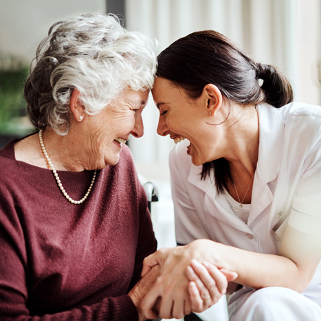 Ein Seniorin und ihre Pflegerin lachen herzhaft zusammen