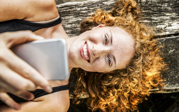 Ein junge Frau genießt lächelnd die Vorzüge von Meine GESUNDHEIT auf ihrem Smartphone.