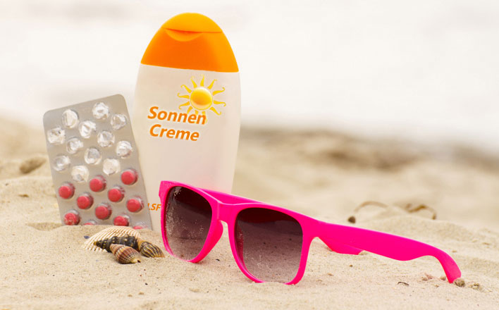 Stillleben Sonnencreme, Tabletten und Sonnenbrille im Sand