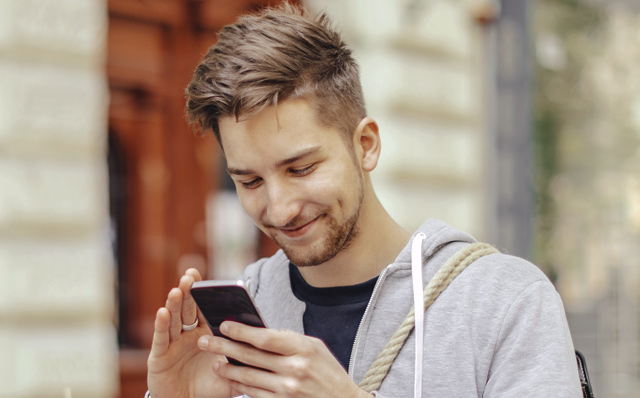 Ein junger Mann freut sich über eine Nachricht, die er auf seinem Handy empfangen hat.