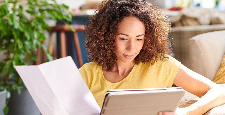 KNAPPSCHAFT Anträge & Formulare.   Eine Frau hält ein Tablet und schaut auf ein Formular der KNAPPSCHAFT und auf ausgedruckte Anträge.