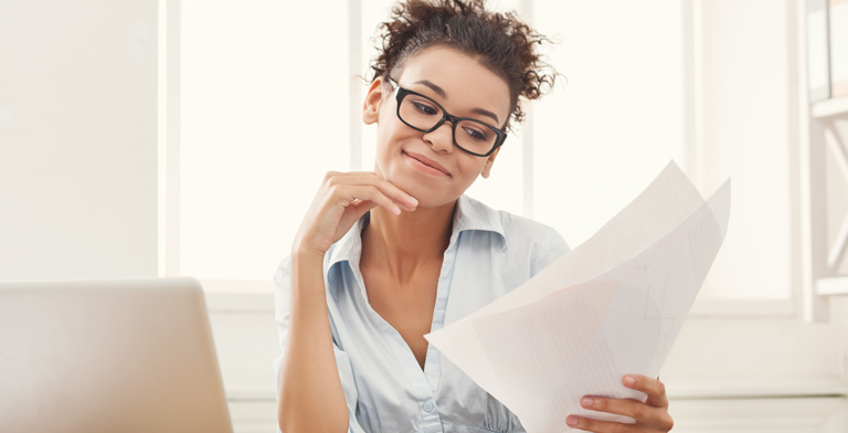 Antrag für die Krankenversicherung. Eine Frau sitzt vor einem Laptop und schaut auf einen ausgedruckten Antrag ihrer Krankenversicherung.