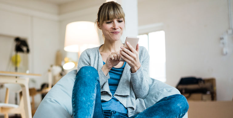 digital.fit - das Wissensportal. Eine Frau sitzt zuhause und nutzt auf ihrem Smartphone das Wissensportal digital.fit.