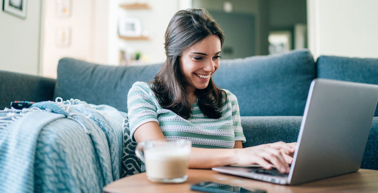 Digitale Services Ihrer Krankenkasse Eine junge Frau sitzt vor ihrem Sofa und nutzt die digitalen Services der KNAPPSCHAFT auf ihrem Laptop.