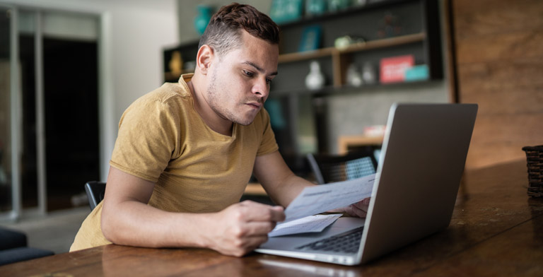 Widersprüche Ein Mann sitzt mit Dokumenten in der Hand vor einem Laptop.
