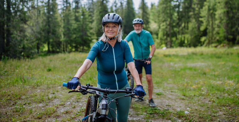 Fit mit der KNAPPSCHAFT GesundTour. Eine älteres Paar mit Fahrrädern in einem Wald nimmt an der GesundTour teil.