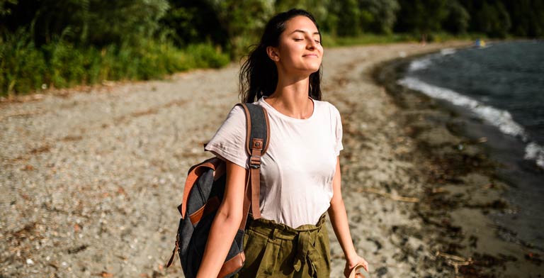 Endlich Nichtraucher werden. Eine junge Frau steht nach der Raucherentwöhnung an einem See und atmet tief durch.