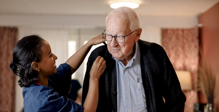 Die Kurzzeitpflege der Pflegekasse. Ein älterer Mann mit einer Pflegerin in einem Pflegeheim in der Kurzzeitpflege der Krankenkasse.