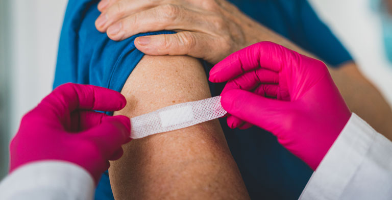 Corona-Impfung und Krankenversicherung. Einer älteren Person wird nach der Corona-Impfung ein Pflaster auf den Arm geklebt.