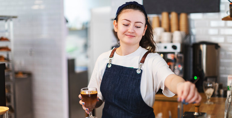 Midijob und Krankenversicherung. Eine junge Barista serviert als Midijobberin Kaffee - sie hat sich über die Krankenversicherung für Midijobber informiert.