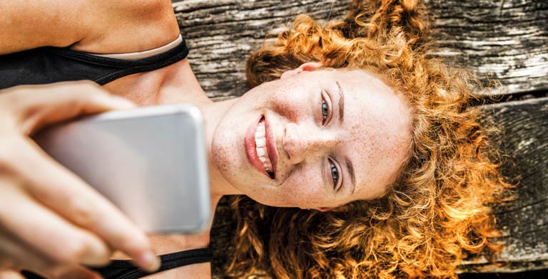 ePA-App – Meine GESUNDHEIT. Eine Frau liegt lächelnd auf einer Bank und nutzt auf dem Smartphone in ihrer Hand die ePA App.