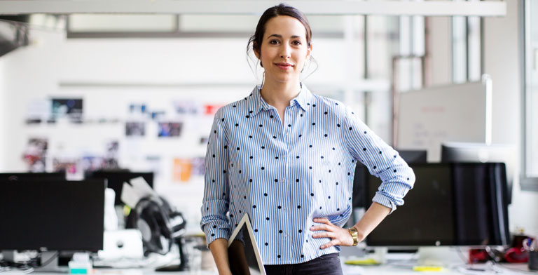 Die KNAPPSCHAFT ist Ihre Krankenkasse in Senftenberg Eine Junge Frau steht in einem Büro und schaut freundlich in die Kamera.