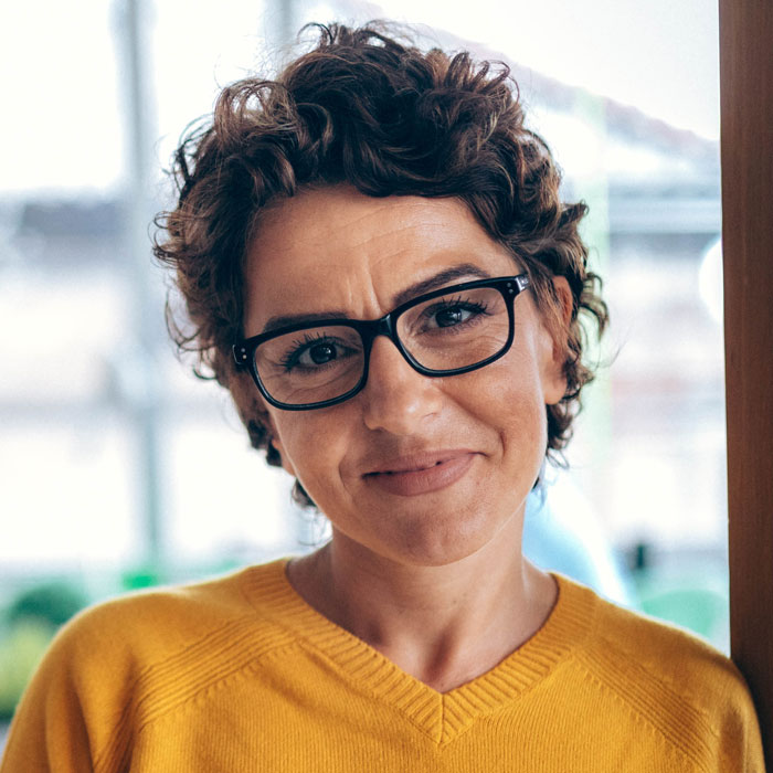 Eine Frau mit Brille und kurzen lockigen Haaren guckt lächelnd in die Kamera. Eine Frau mit Brille und kurzen lockigen Haaren guckt lächelnd in die Kamera.