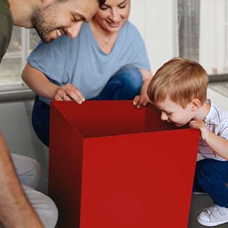 Ein kleiner Junge schaut lächelnd in ein großes rotes Paket, während seine Mama und sein Papa neben ihm auf dem Boden sitzen. Ein kleiner Junge schaut lächelnd in ein großes rotes Paket, während seine Mama und sein Papa neben ihm auf dem Boden sitzen.